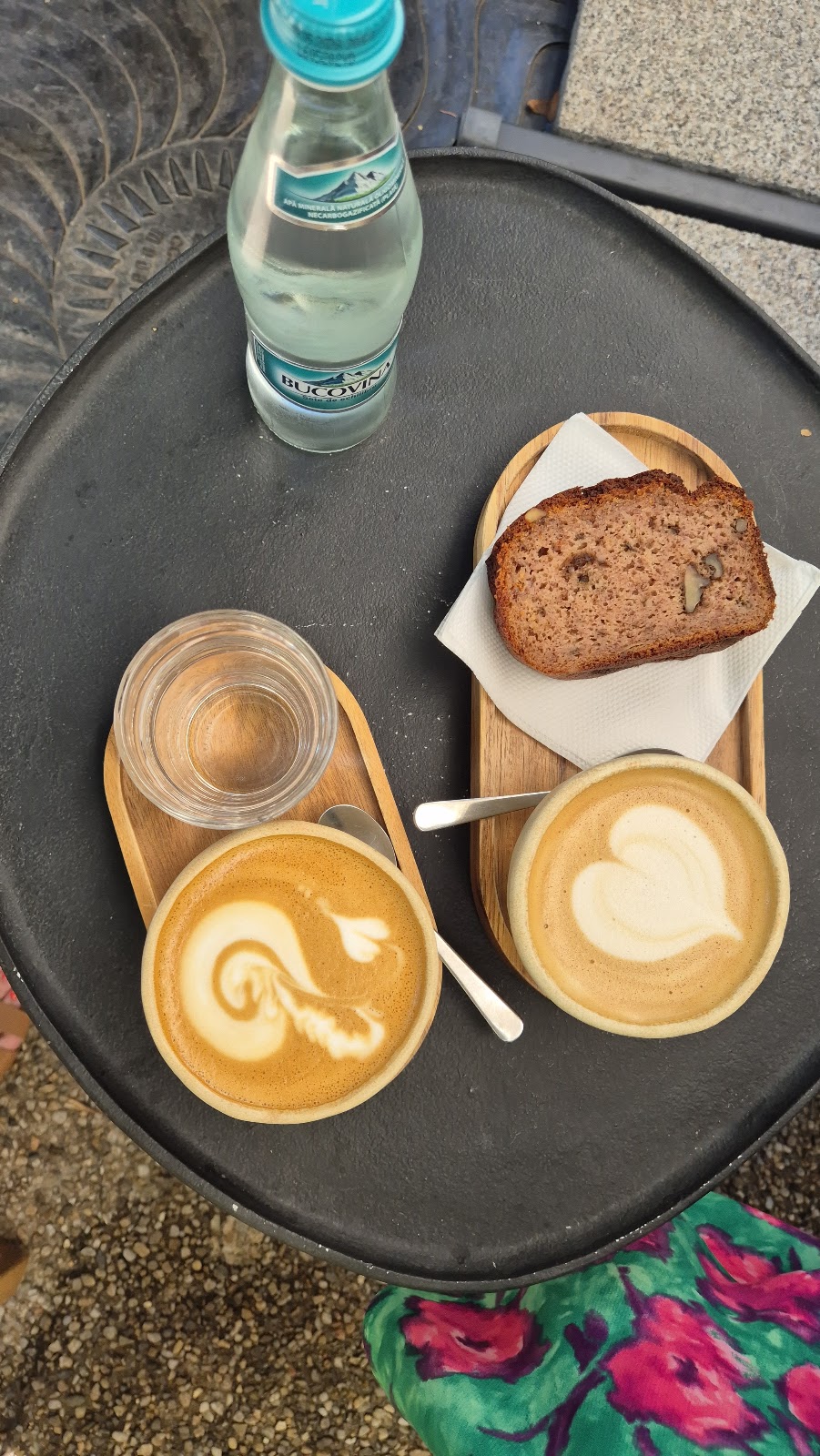 Banana bread și două cafele cu lapte pe o masă din curte
