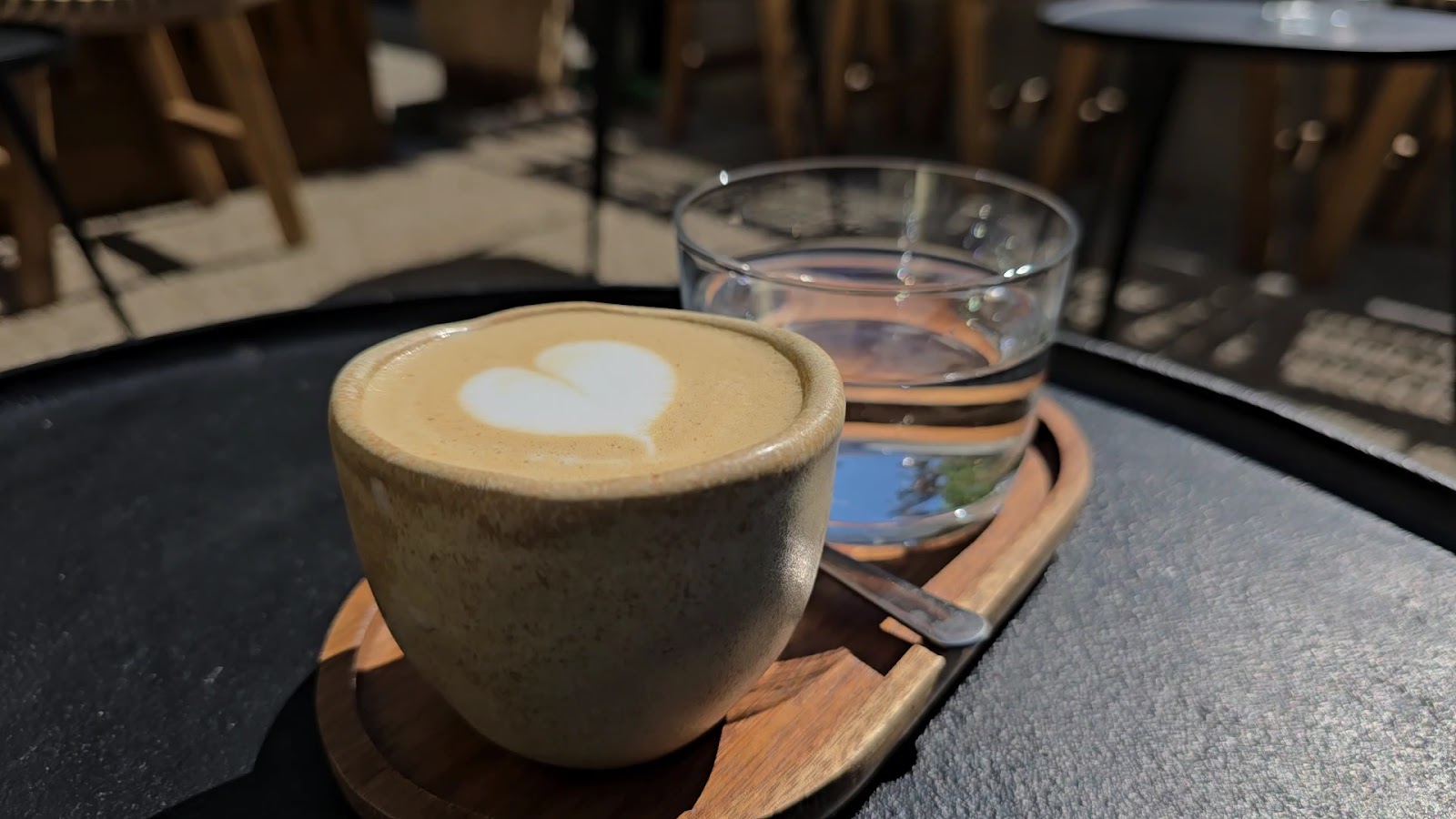 Flat white în ceașcă de ceramică și pahar de apă, pe terasa din curte